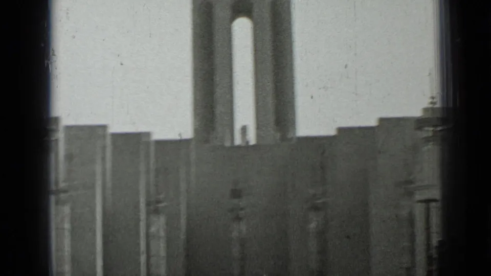 The frame shifts away from the women to the church exterior, showing steps, walls, and tall vertical forms in soft focus.
