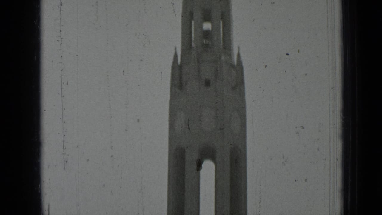 Upper portion of a Gothic-style bell tower seen against a pale sky with dark frame edges.