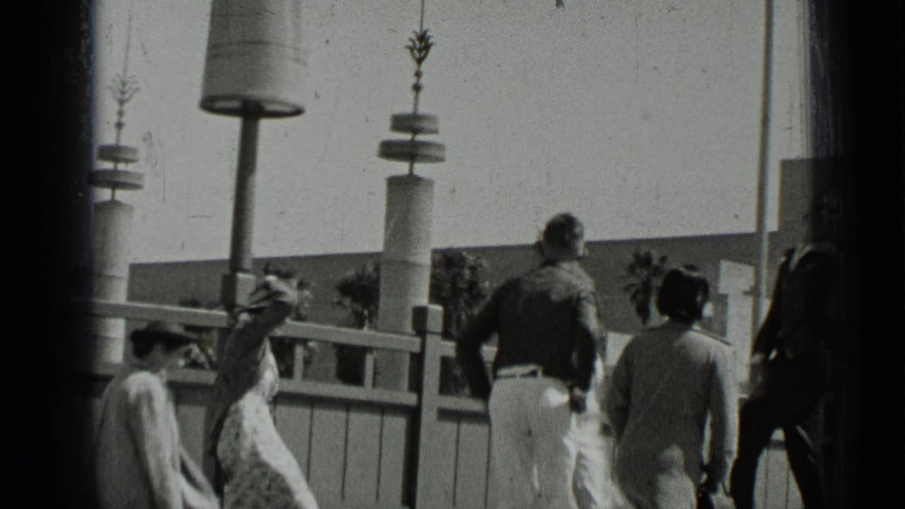 1937 San Francisco home-movie frame showing men and women walking near railings and tall modern lampposts.