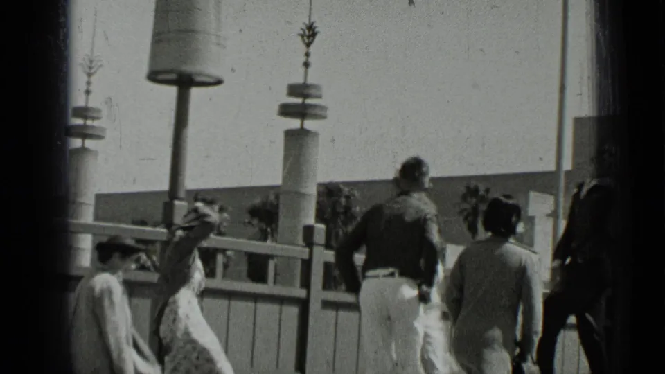 1937 San Francisco home-movie frame showing men and women walking near railings and tall modern lampposts.