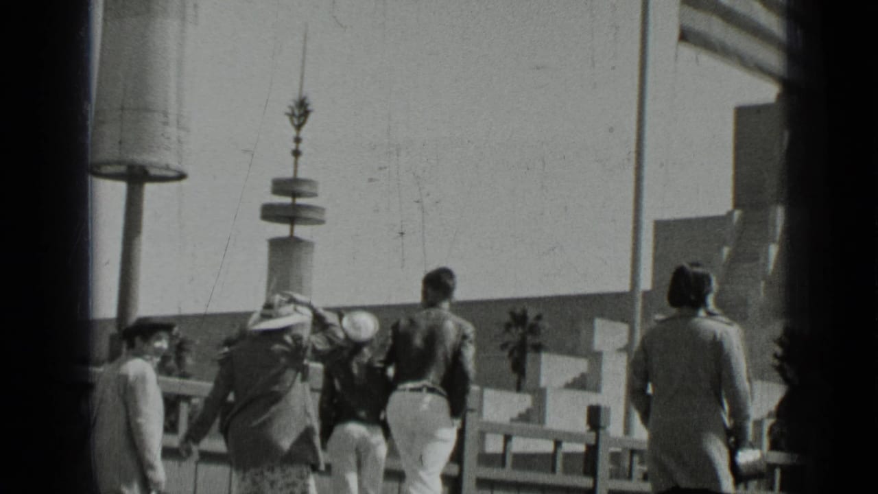 Several people walk away from the camera near railings and lampposts.