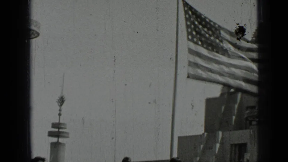 1937 San Francisco frame with an American flag blowing beside railings, a lamppost, and partial building forms.
