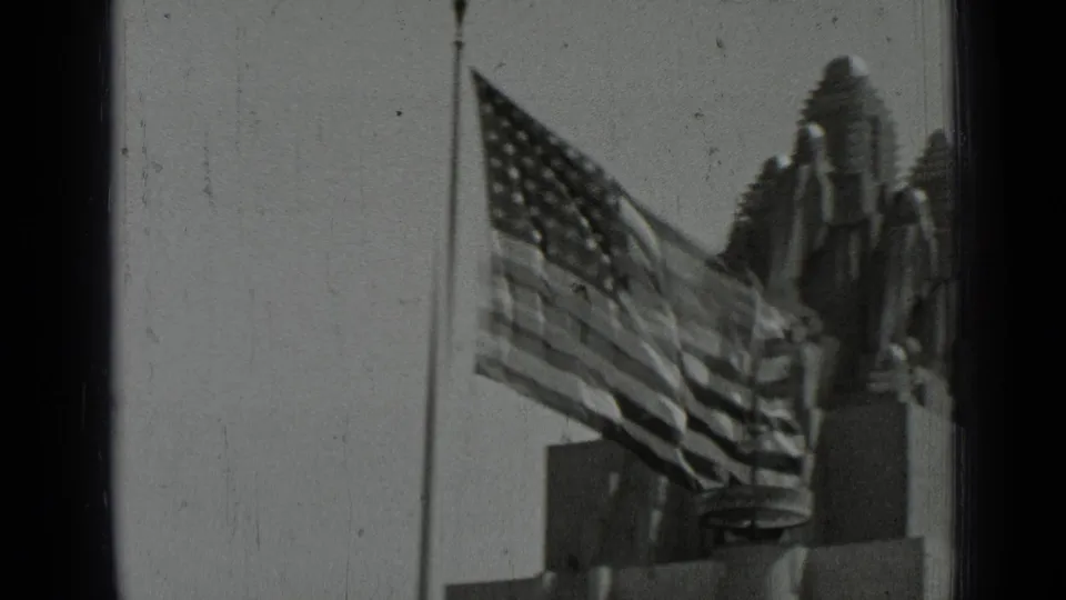 1937 San Francisco home-movie frame focused on a large American flag with buildings and a statue-like form behind it.