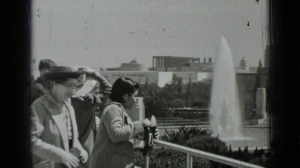 1937 San Francisco home-movie frame showing visitors near a balcony rail, with a large fountain and civic-looking buildings beyond.