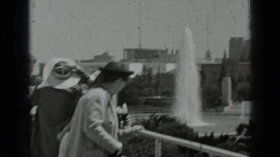 Black-and-white 8mm frame from 1937 San Francisco showing visitors in hats at a balcony, looking toward a fountain and surrounding grounds.