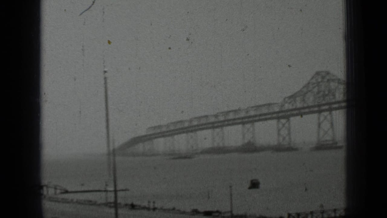 Bridge span over water with a thin pole and waterfront edge in the foreground.
