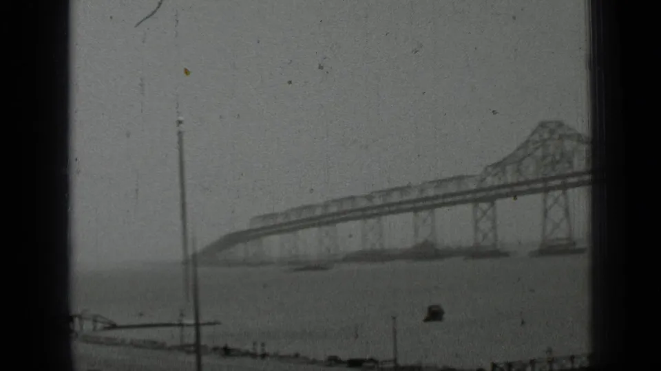 San Francisco bridge view over bay water, with a foreground pole and promenade edge visible in the 1937 8mm footage.