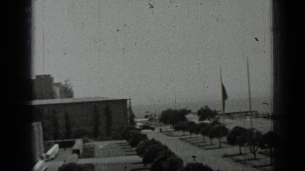 1937 San Francisco home-movie view across low buildings, trees, and a walkway, partly obscured by dark 8mm frame edges.