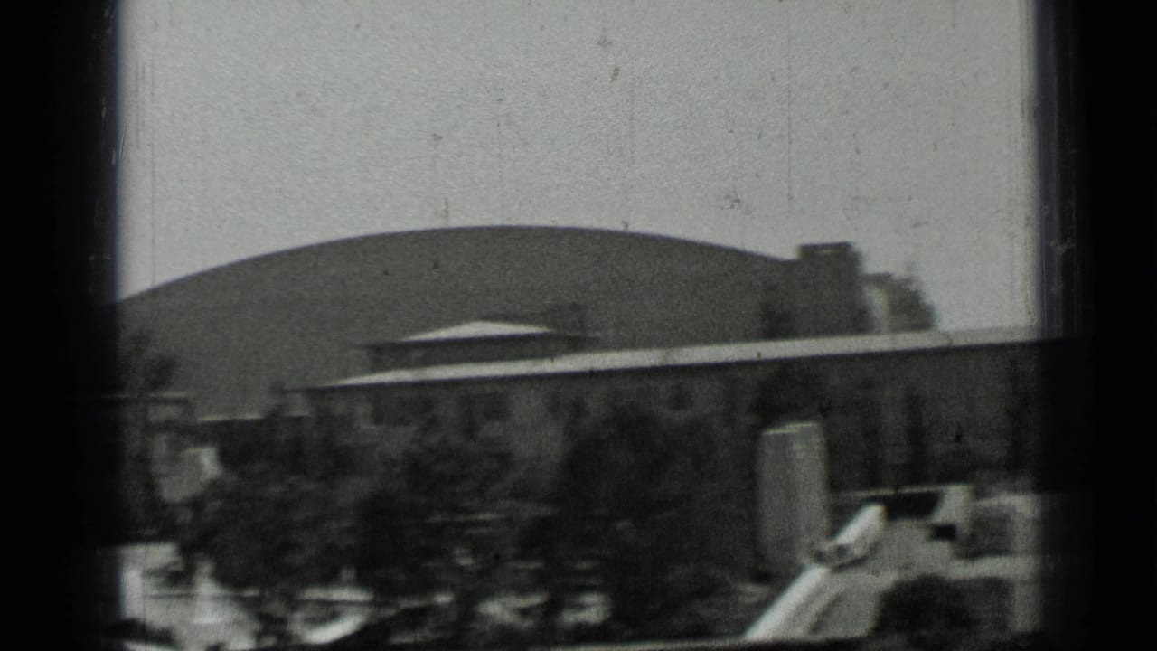 Large domed building behind low structures and trees.