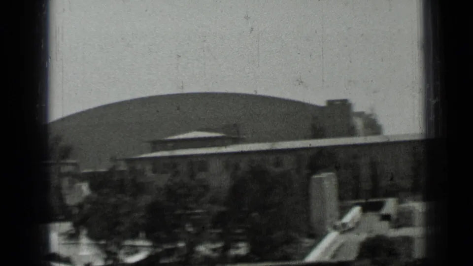 A large domed structure rises behind low San Francisco buildings and trees in soft monochrome 8mm footage.