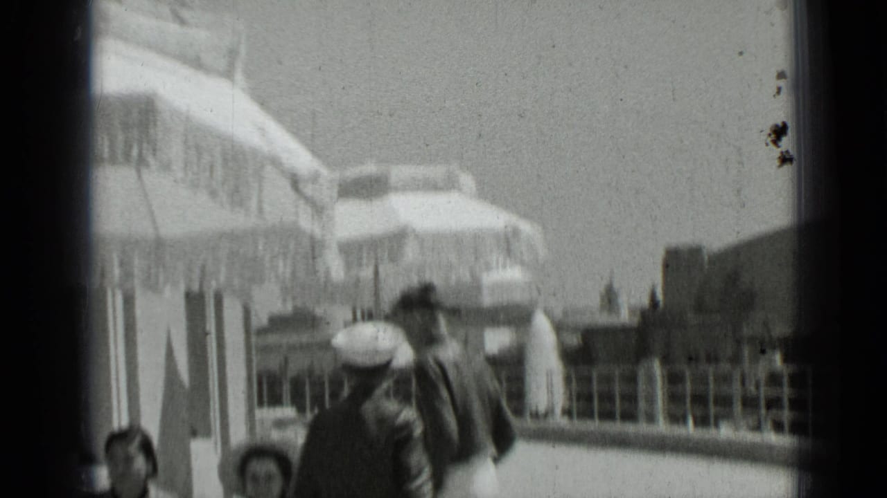 People pass under large patio umbrellas beside a building and railing.