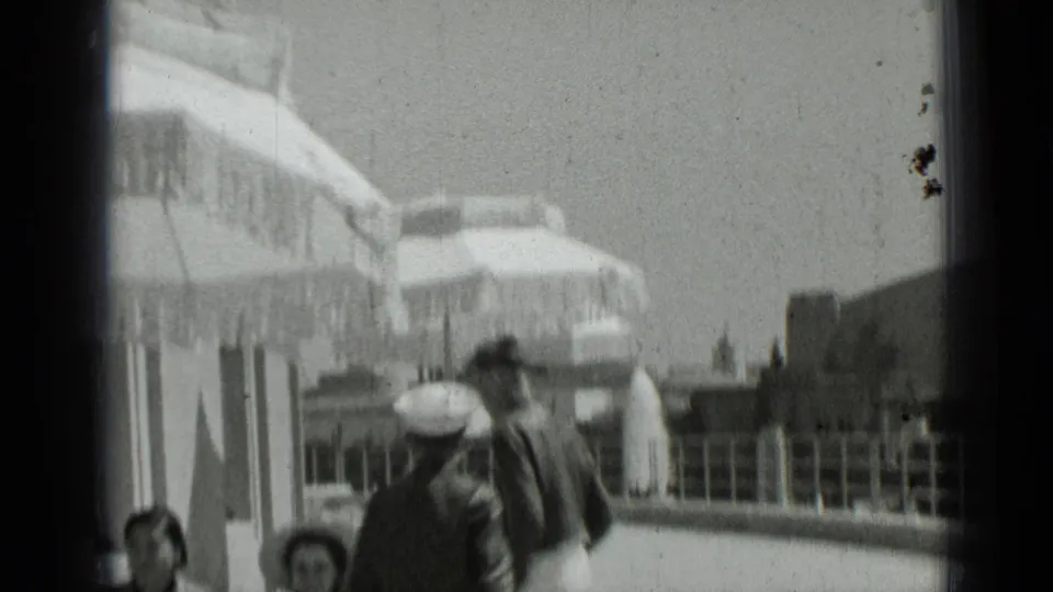 1937 San Francisco home-movie frame showing people moving through a sunny patio area beneath large umbrellas.