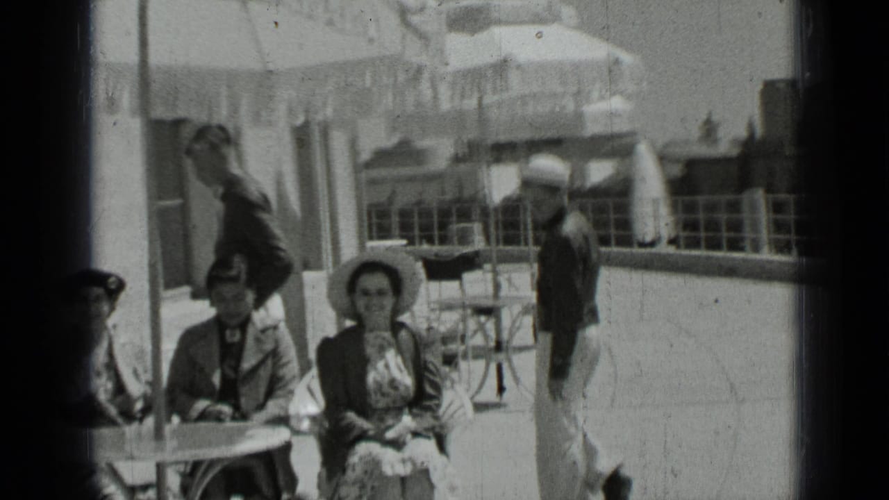 Adults sit at a patio table while a sailor stands nearby.