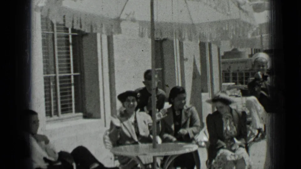 Several adults sit around a round patio table beneath an umbrella, with a sailor standing nearby in the 1937 San Francisco clip.