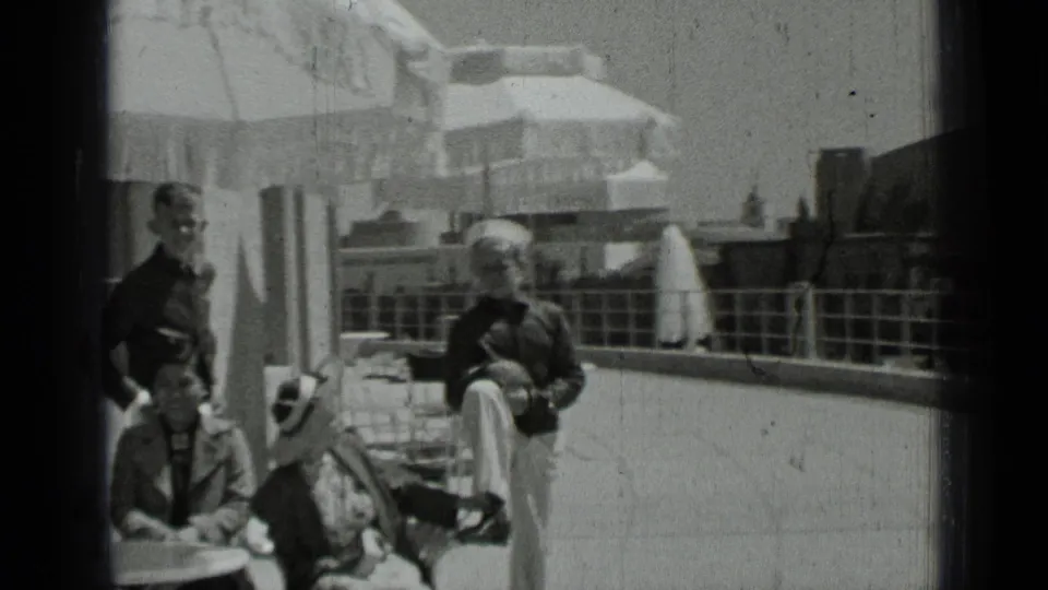 Black-and-white 8mm frame showing men and seated companions near a patio table and railing, consistent with the 1937 San Francisco clip metadata.