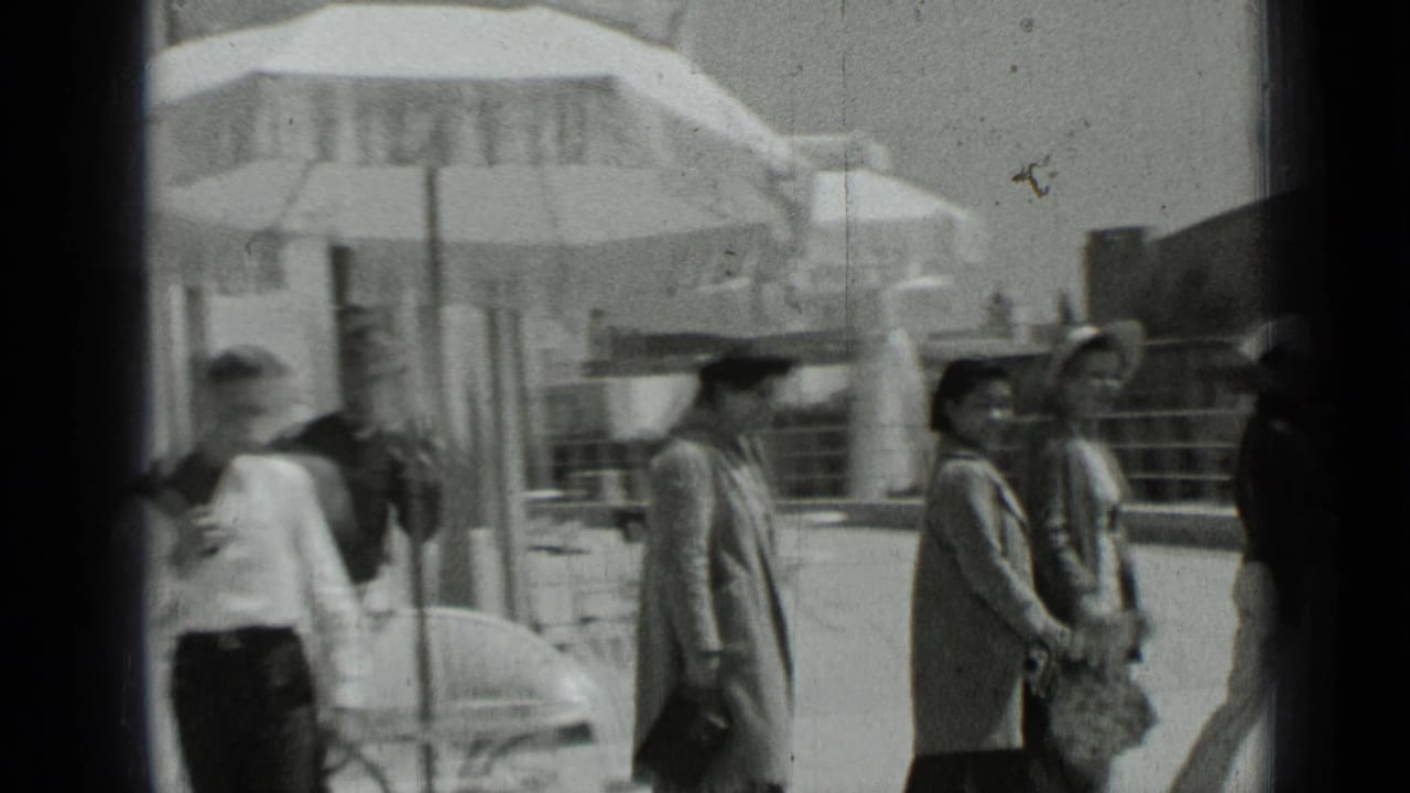 Several people walk along a patio beside umbrellas and a railing.