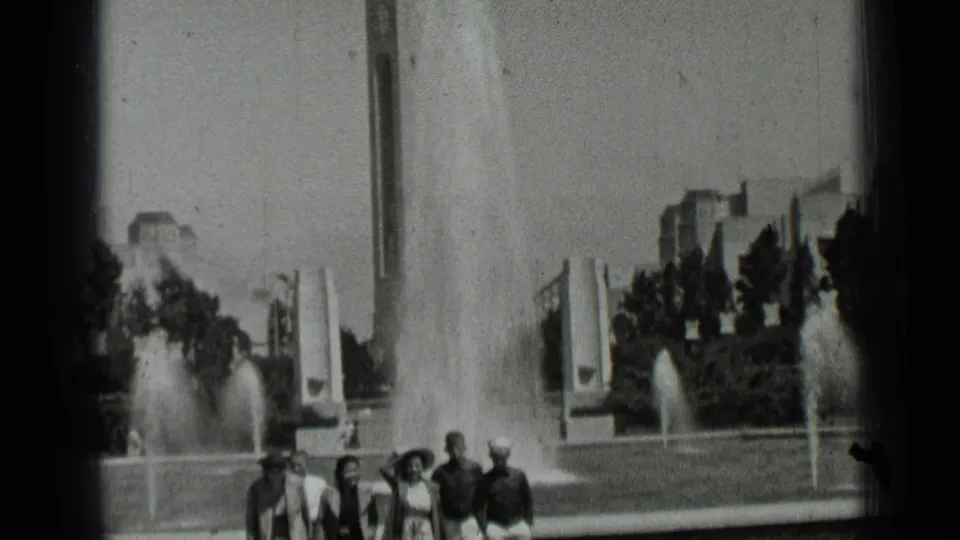 1937 San Francisco home-movie frame showing young adults walking near fountain jets and modernist park structures.