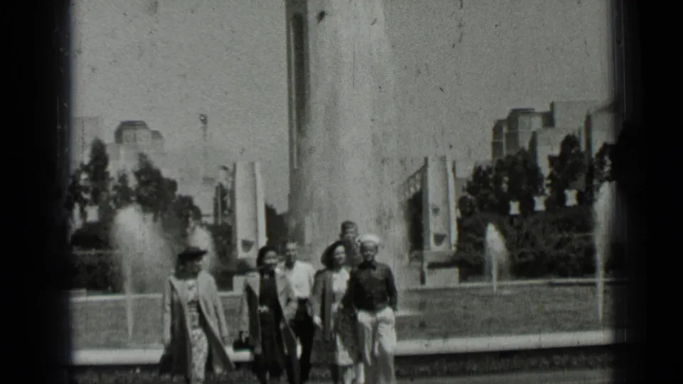 1937 San Francisco park scene with a small group in period clothing walking toward the camera by fountain pools.
