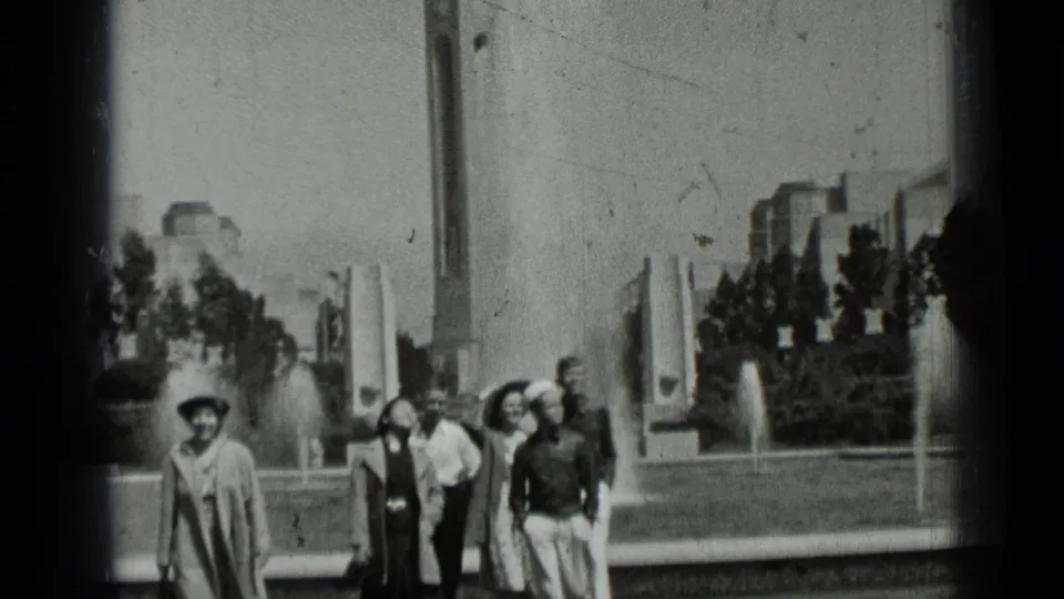 Black-and-white 1937 San Francisco frame showing visitors walking together past fountains and landscaped park features.
