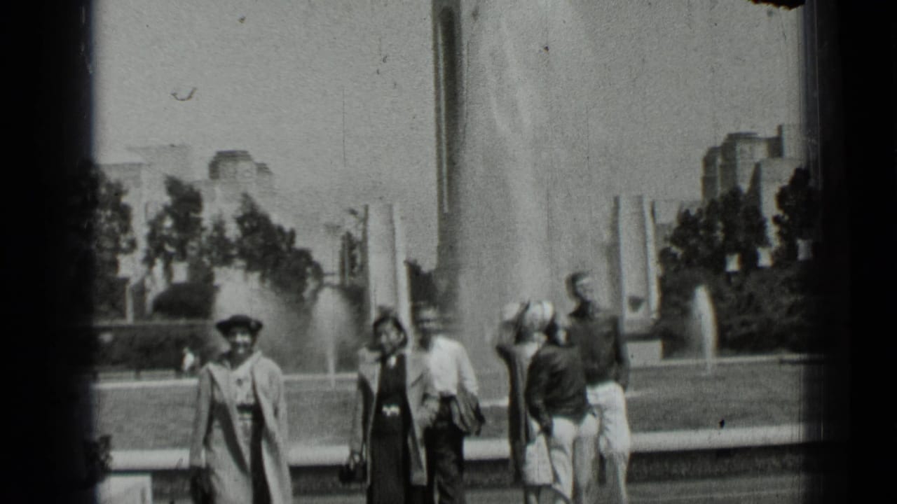 People walking near a fountain in a landscaped city park.