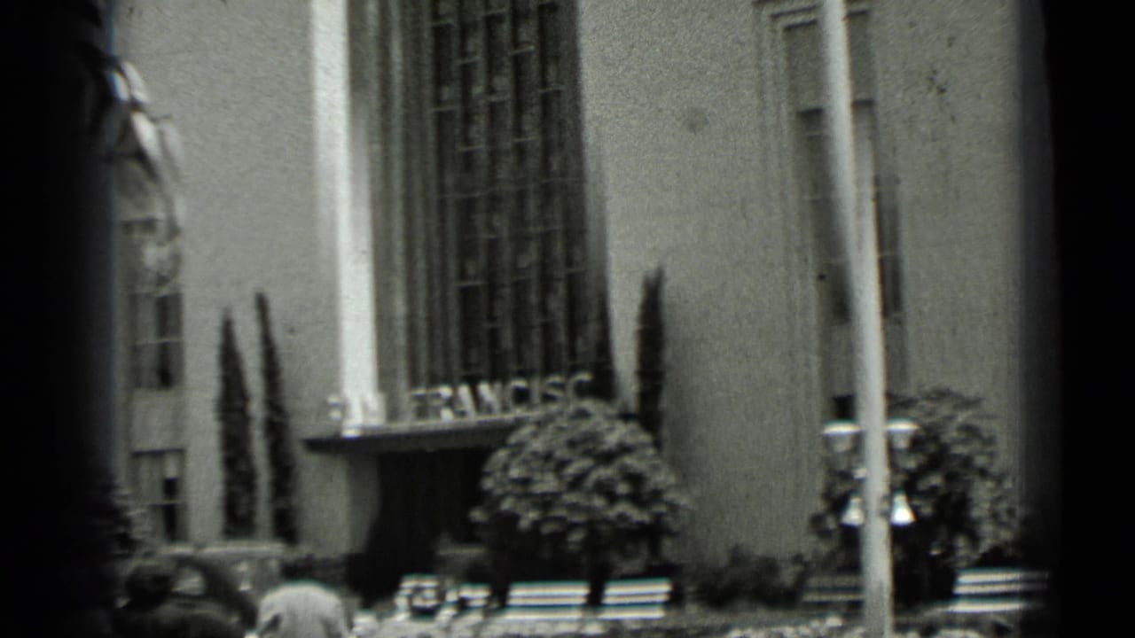 Pedestrians pass a grand building with San Francisco lettering and vertical columns.
