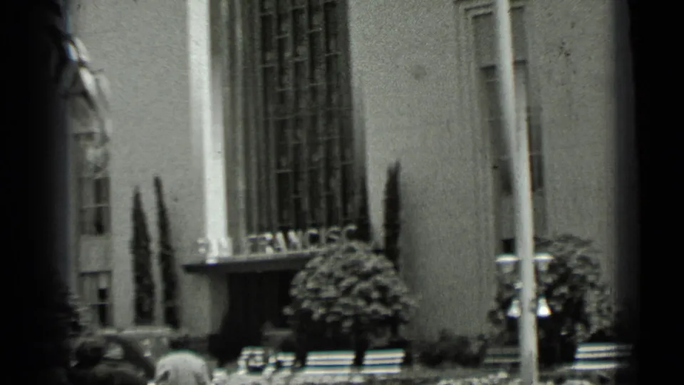 1937 San Francisco home-movie frame showing pedestrians near a grand columned building with San Francisco lettering above the entrance.