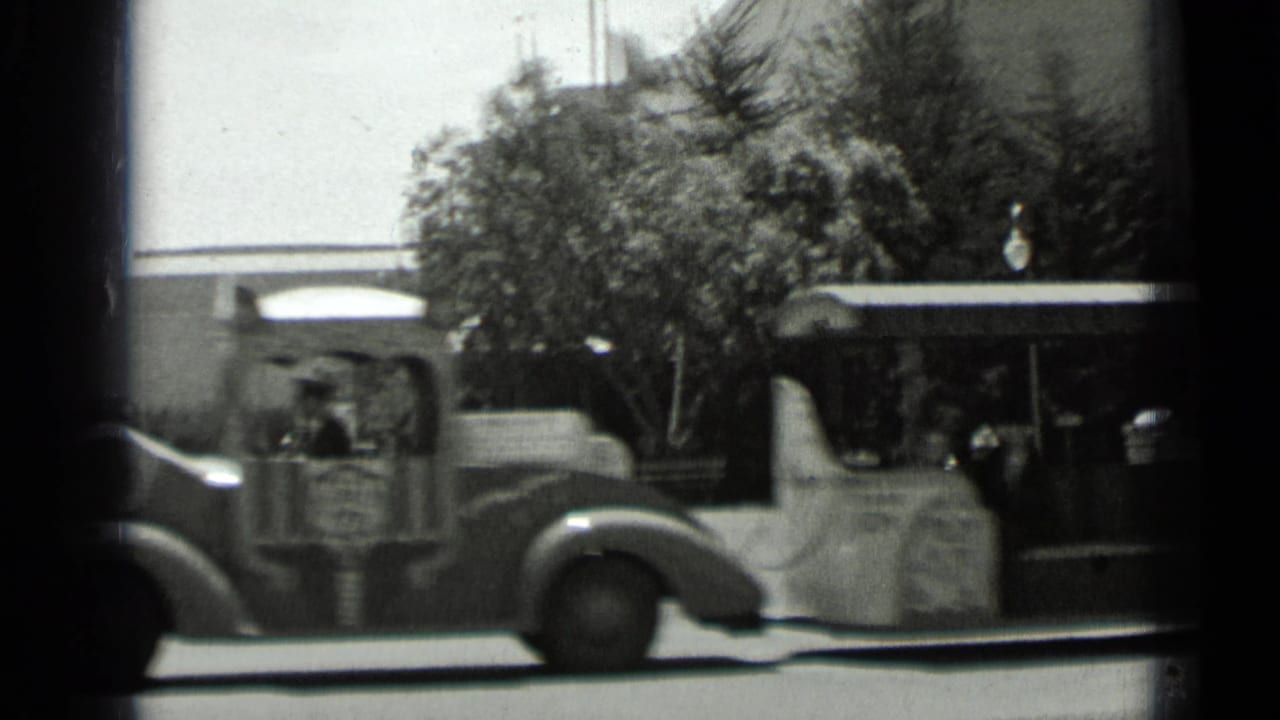 Street vehicle passing in front of trees and a low building.