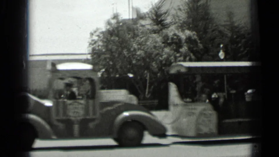 Black-and-white San Francisco street view with a passenger or service vehicle moving past trees and a low building in 1937 footage.