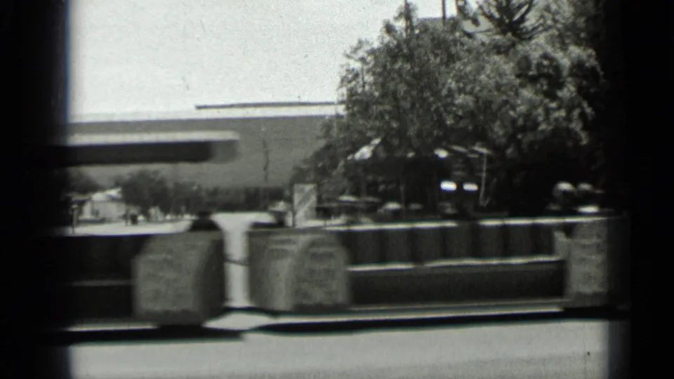 1937 San Francisco exterior with large planters, leafy trees, benches, and a building facade seen from a moving 8mm camera.