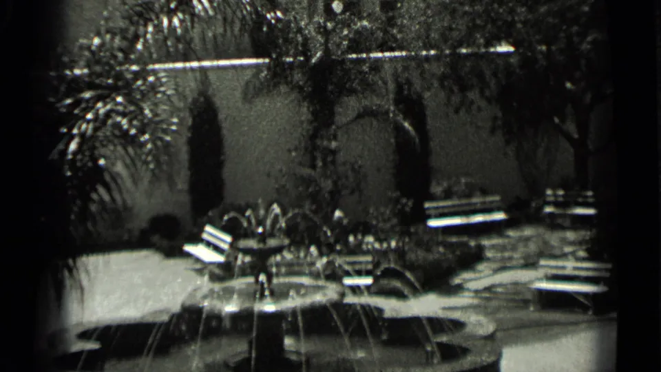 1937 San Francisco home-movie frame showing a courtyard fountain, benches, palm plantings, shrubs, and a stucco garden wall.