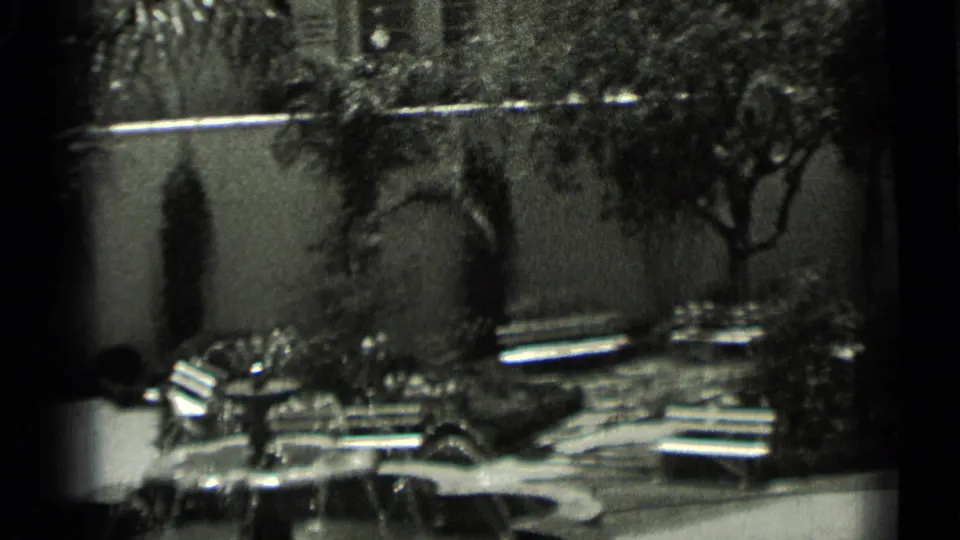 1937 San Francisco home-movie frame with fountain foreground, benches, palm plantings, shrubs, and arched forms along a courtyard wall.