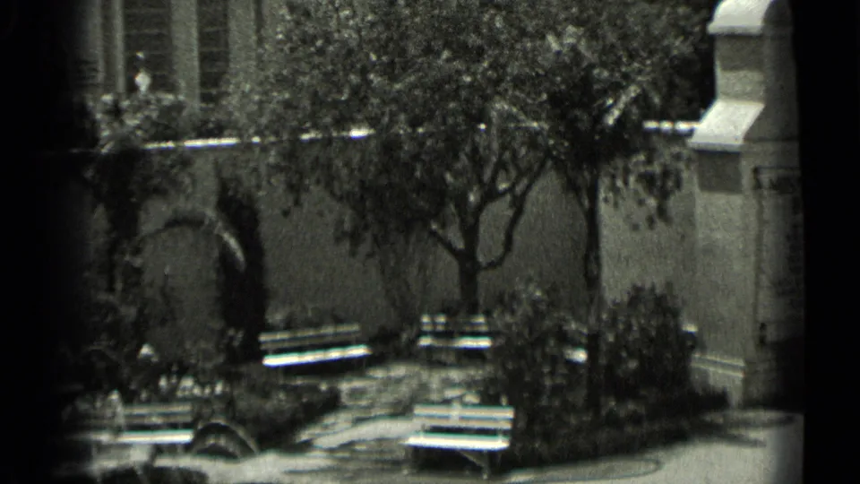 1937 San Francisco frame showing benches and planting beds before a stucco wall, with an arched opening and part of a monument visible at right.