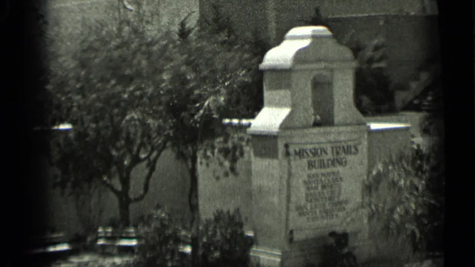 1937 San Francisco home-movie frame showing a stone Mission Trails Building sign with trees, shrubs, and soft film borders.