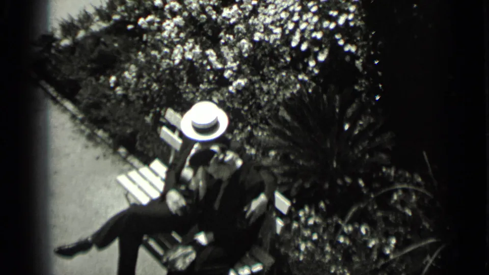 High-angle 1937 San Francisco frame showing a man in a white hat and dark suit seated on a park bench among foliage.