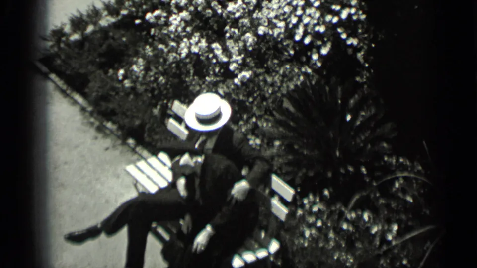 High-angle black-and-white view of a couple on a bench in a San Francisco courtyard, surrounded by clipped greenery.