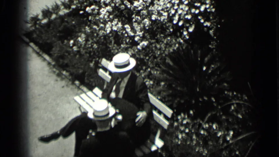 1930s black-and-white home-movie still of a couple sitting closely on a courtyard bench in San Francisco.