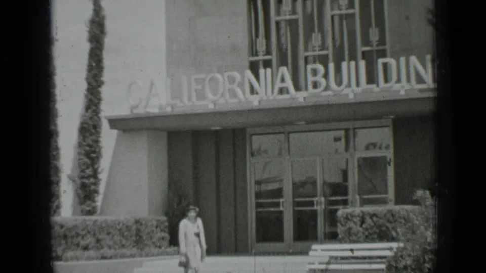 1937 San Francisco 8mm frame showing the California Building sign above glass doors as a pedestrian passes the hedged entrance.