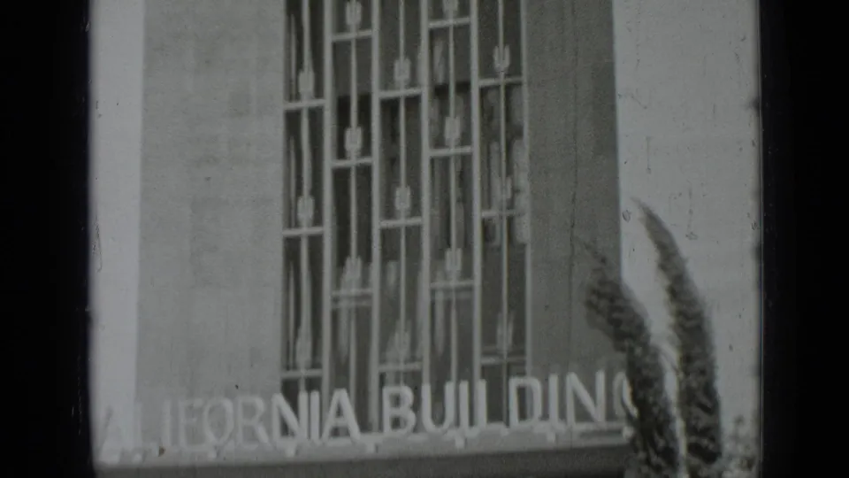 Tight black-and-white 8mm frame of the California Building facade, emphasizing vertical window grilles and partial signage.