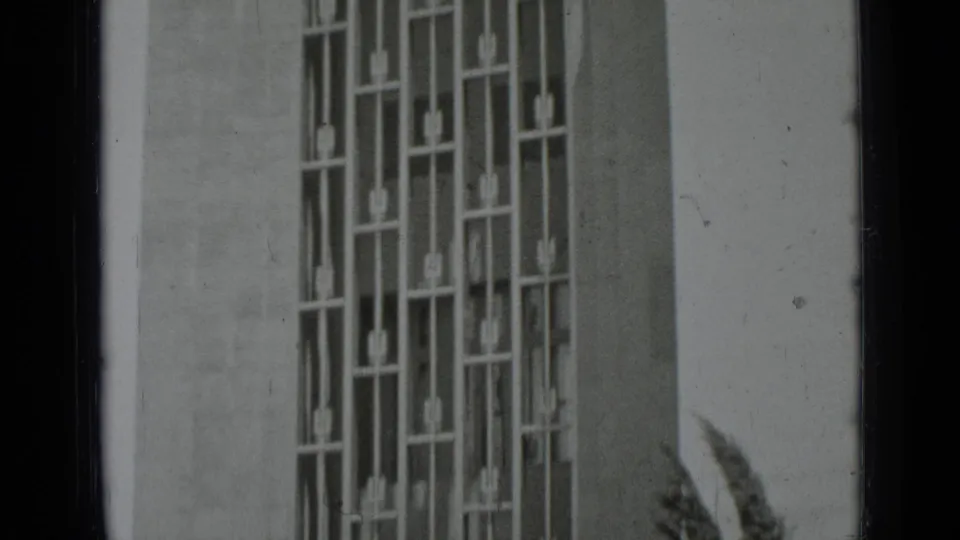 Black-and-white 1937 San Francisco frame showing a tall geometric metal window grille on a pale building wall.