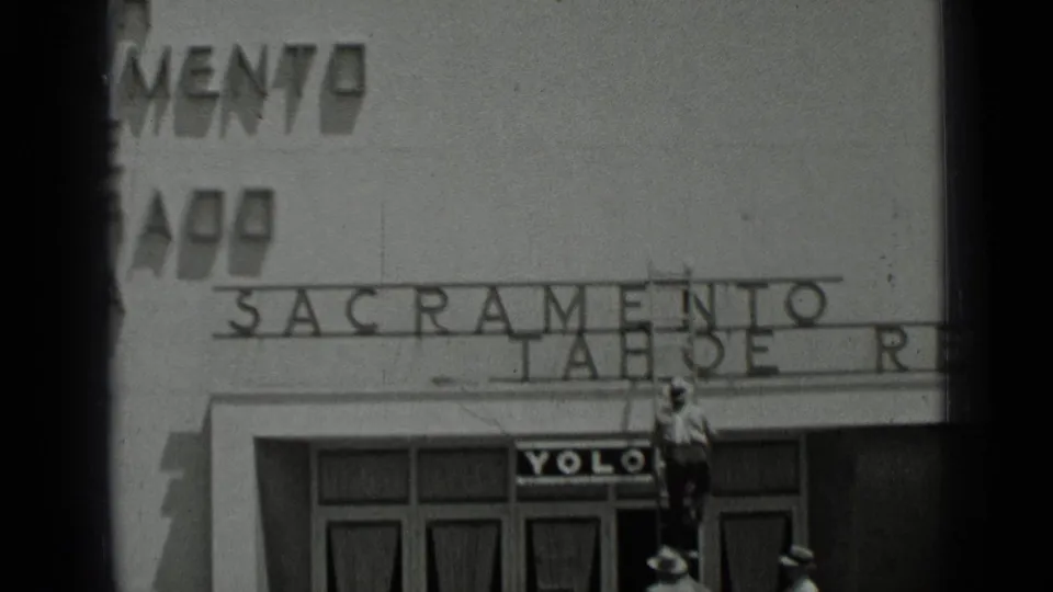 1937 San Francisco frame showing a man on a ladder working near large Sacramento and Tahoe facade lettering above a storefront with a YOLO sign.
