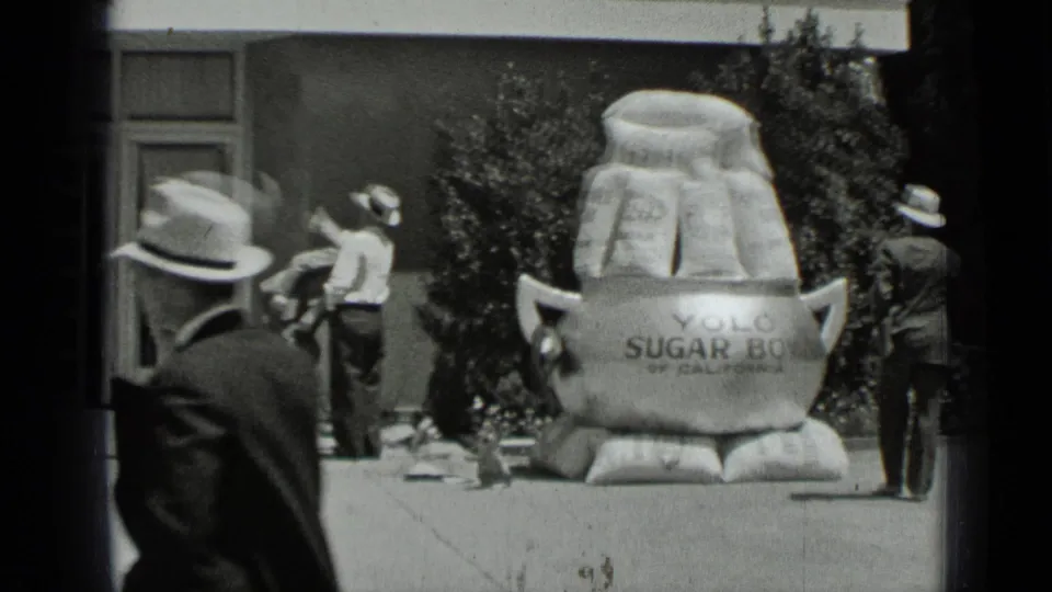 1937 San Francisco home-movie frame showing men near a storefront with a large YOLO sugar-bag promotional display.