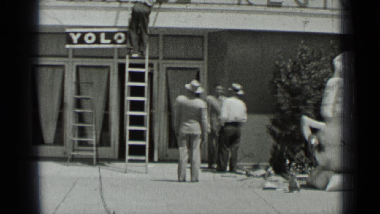 Man on ladder above a YOLO storefront while three men stand on the sidewalk.