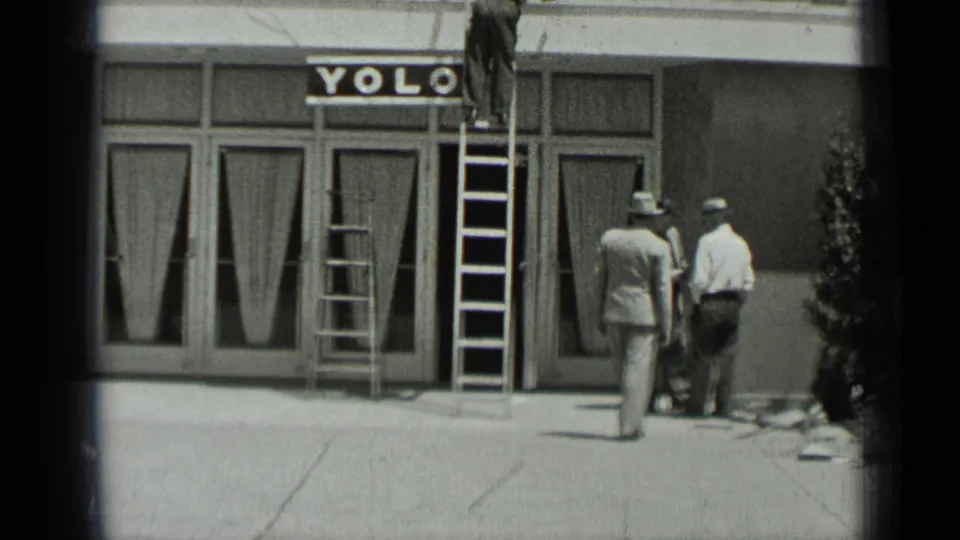 The storefront sign and ladders remain in view as two men stand near the entrance and a worker is partly visible above.