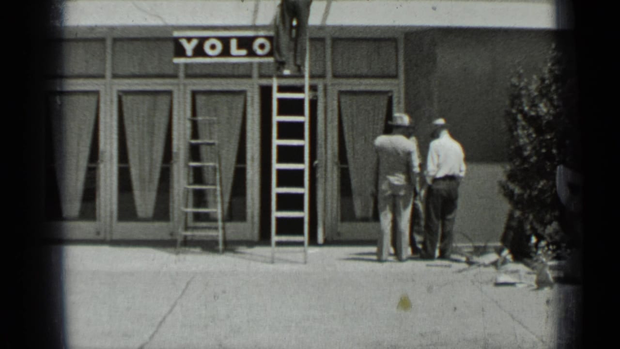 Men stand near ladders outside a Yolo storefront with a sidewalk in front.