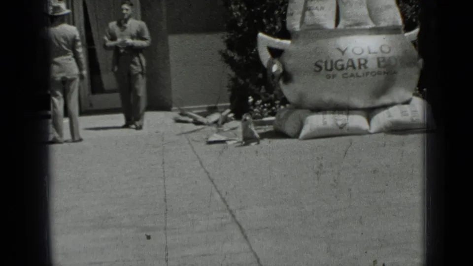 1937 San Francisco home-movie frame showing two men by an oversized sugar bowl display labeled for Yolo Sugar Bowl of California.