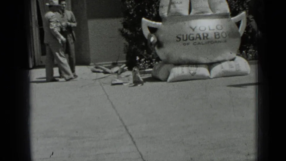 A suited man stands near the person-sized sugar bowl prop in the 1937 San Francisco sidewalk scene.
