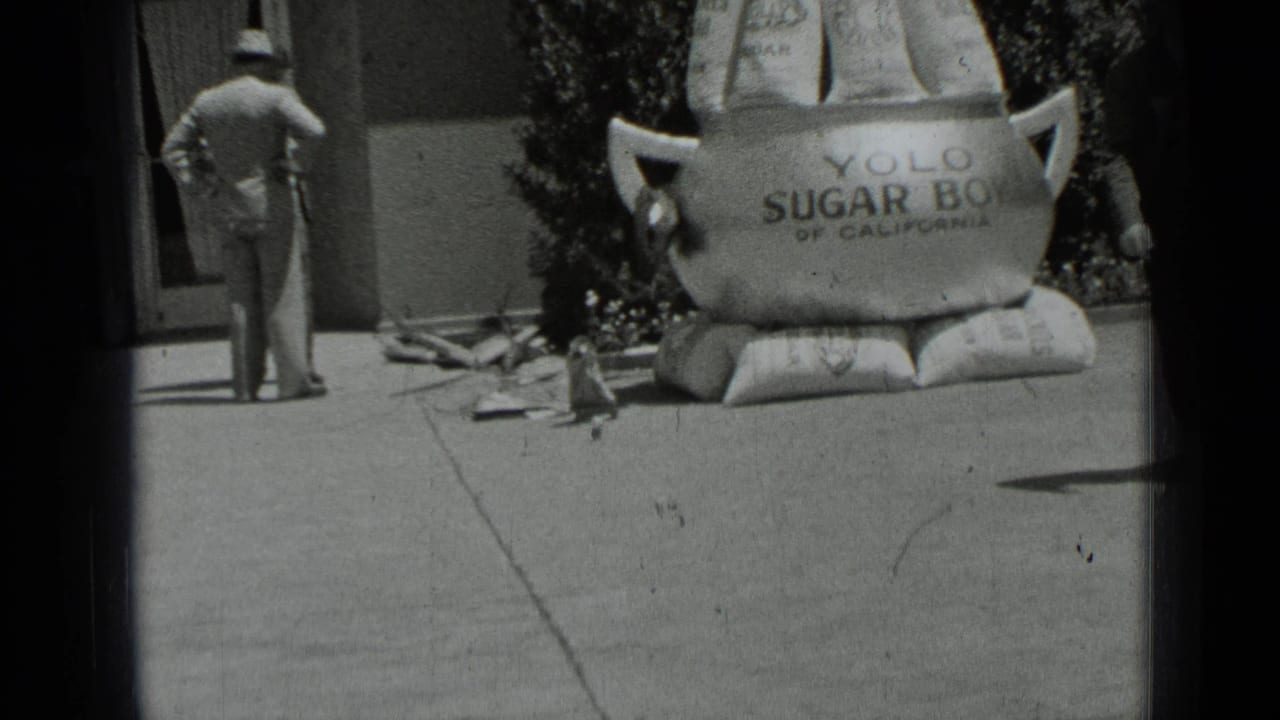 A man in a hat stands with his back to the camera near the oversized Yolo Sugar Bowl display on a San Francisco sidewalk.