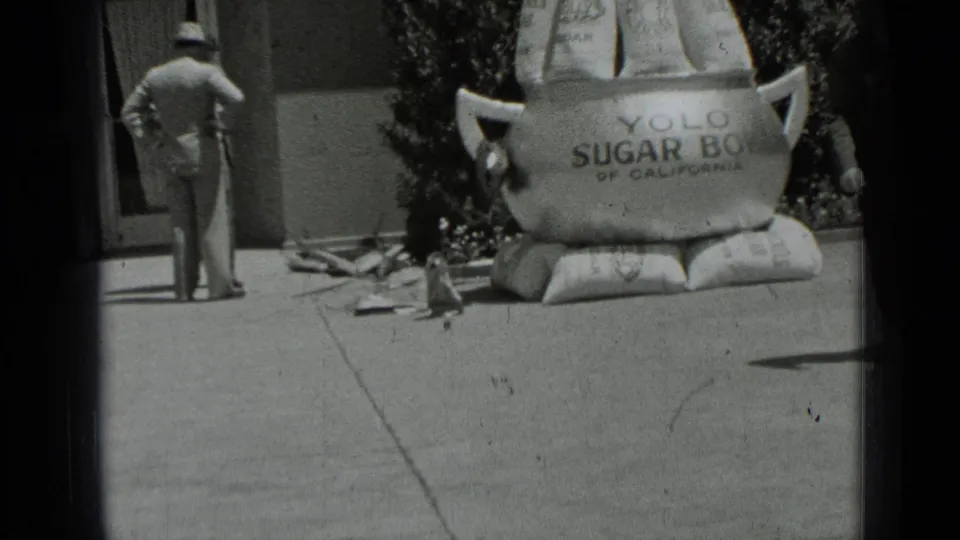 A man in a hat stands with his back to the camera near the oversized Yolo Sugar Bowl display on a San Francisco sidewalk.