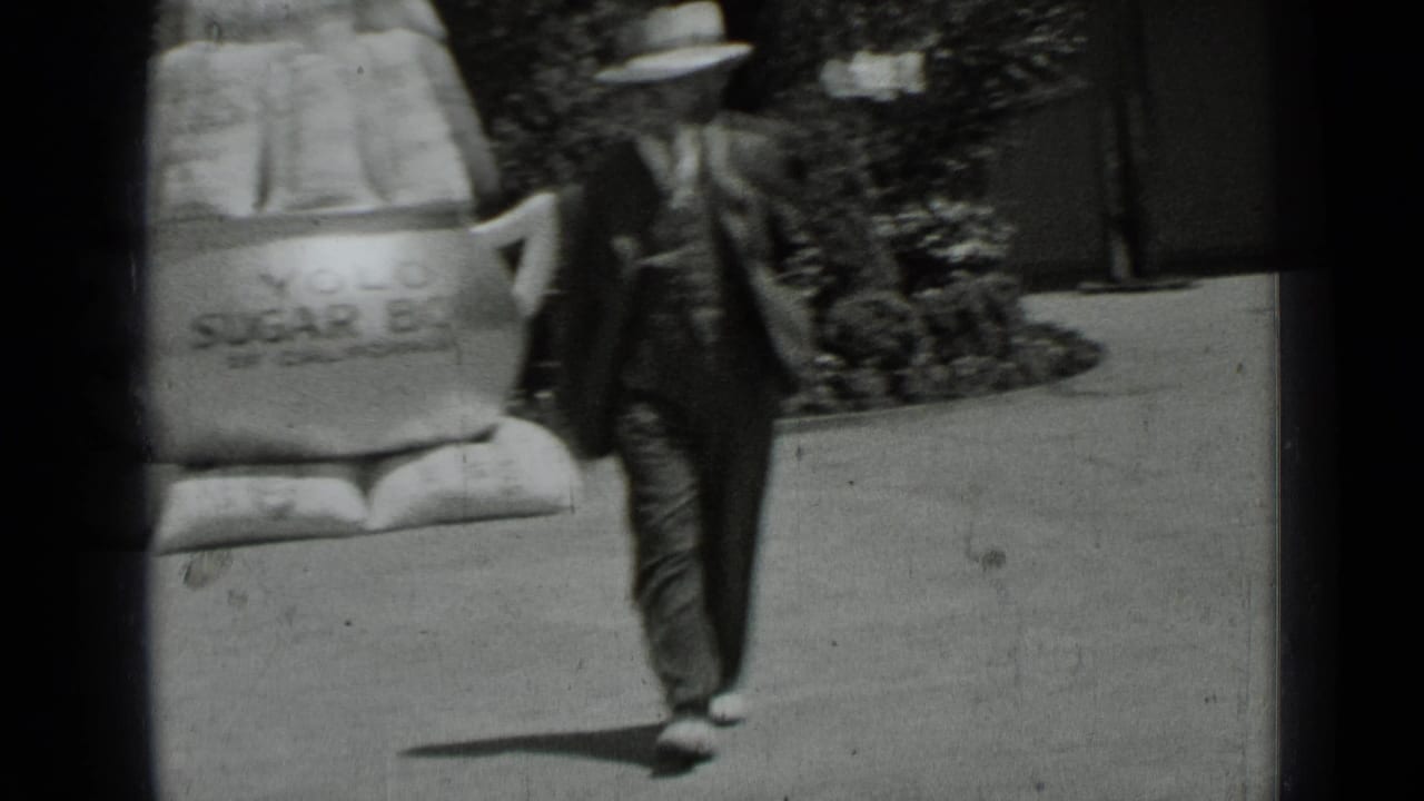 A blurred 1937 San Francisco frame shows a man in a hat walking past the oversized sugar bowl prop and shrub-lined sidewalk.