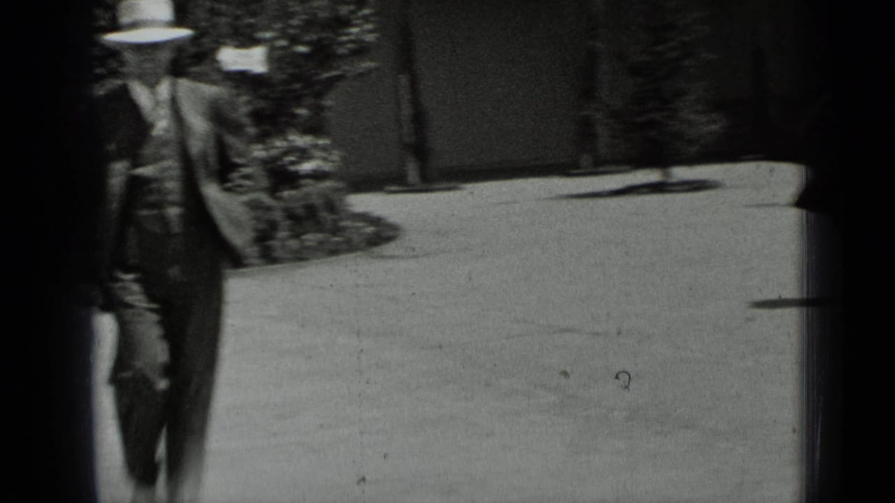 In 1937 San Francisco home-movie footage, a man in a suit and fedora walks through a sunlit garden courtyard.
